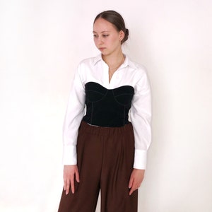 May include: A white button-down shirt with a black corset top and brown wide-leg pants.