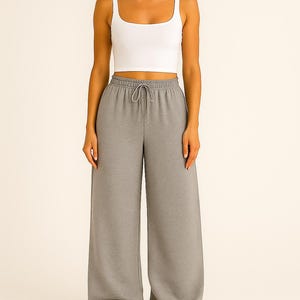 May include: A white square-neck crop top paired with gray wide-leg sweatpants. The sweatpants have a drawstring waist. The outfit is casual and comfortable, suitable for lounging or everyday wear.