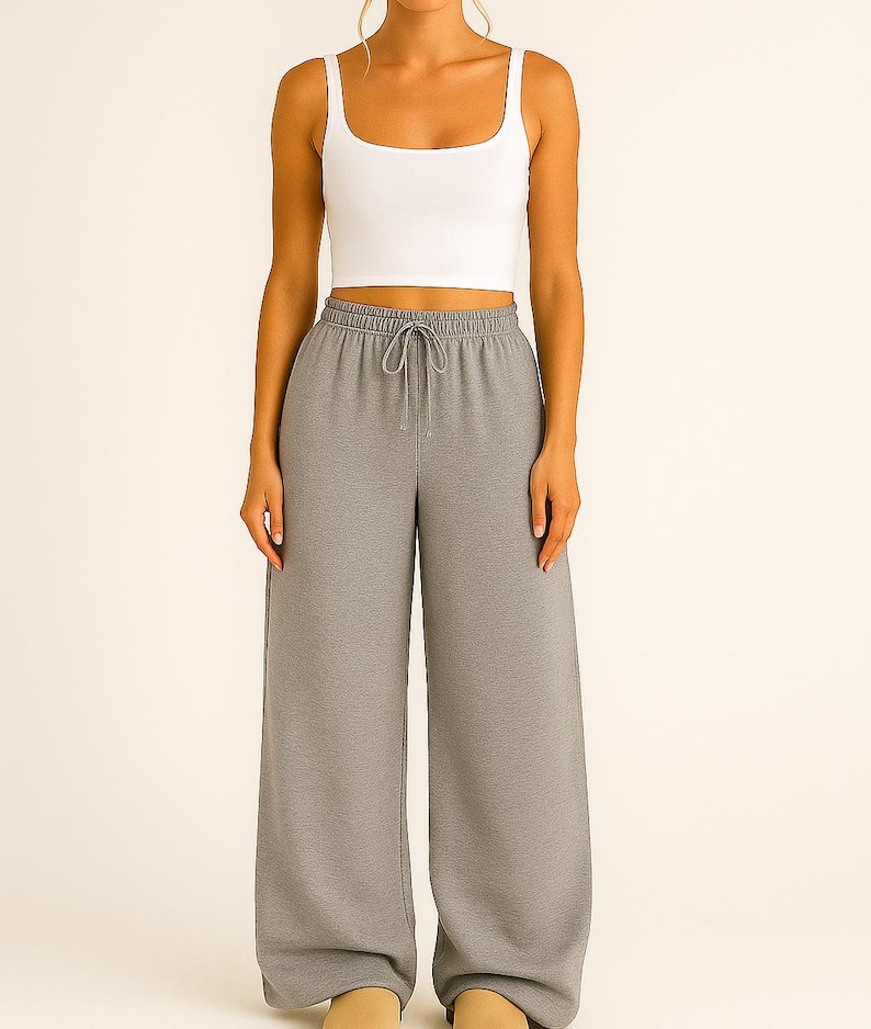 May include: A white square-neck crop top paired with gray wide-leg sweatpants. The sweatpants have a drawstring waist. The outfit is casual and comfortable, suitable for lounging or everyday wear.