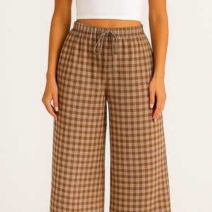 May include: A white crop top paired with brown and tan plaid wide-leg pants. The pants have a drawstring waist. The outfit is casual and comfortable, suitable for everyday wear. The pants have a classic gingham pattern.