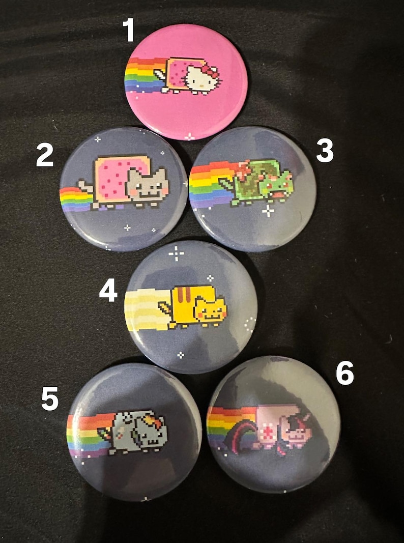 May include: Six round buttons with different pixelated cat images. Each button has a rainbow and a dark blue background with white stars. The cats are wearing different costumes, including a pink dress, a slice of bread, a green dinosaur costume, a yellow Pikachu costume, a blue unicorn costume, and a pink unicorn costume.