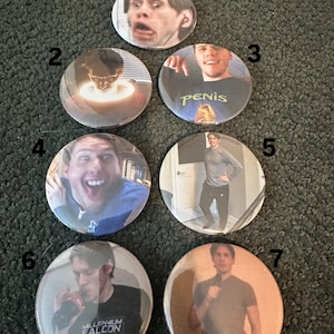 May include: Seven round buttons with different images of a person. The buttons are arranged in a circle on a brown carpet. The buttons are all the same size and have a white border.