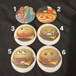 May include: Six round buttons with different images. The first button has a cartoon image of two people in a video game. The second button has a cartoon image of a pizza. The third, fourth, fifth, and sixth buttons have cartoon images of hamburgers with different facial expressions.