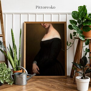 Può includere: Un dipinto incorniciato di una donna che indossa un abito nero con un colletto bianco. La donna guarda in basso e i suoi capelli sono tirati indietro. Il dipinto è posto contro un muro bianco con piante in primo piano.