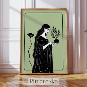 May include: Black and white illustration of a woman in a long dress holding a potted plant. The artwork has a light green background and is framed in a gold-colored frame. The word "Pittoresko" is printed at the bottom.