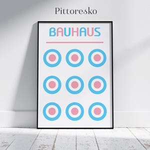 Puede incluir: Un póster enmarcado en negro con el texto "BAUHHAUS" en letras rosas. El póster presenta un patrón de nueve círculos rosas y azules.