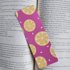 May include: Pink bookmark with a repeating pattern of yellow lemons on a pink background. The lemons have a white outline and a white center with a yellow starburst pattern.