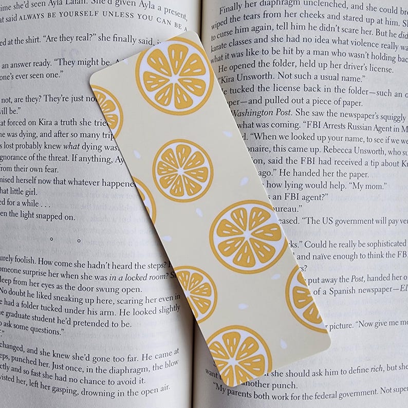 May include: A yellow and white bookmark with a lemon pattern. The bookmark has the text "FBI Arrests Russian Agent in Moscow" printed on it.