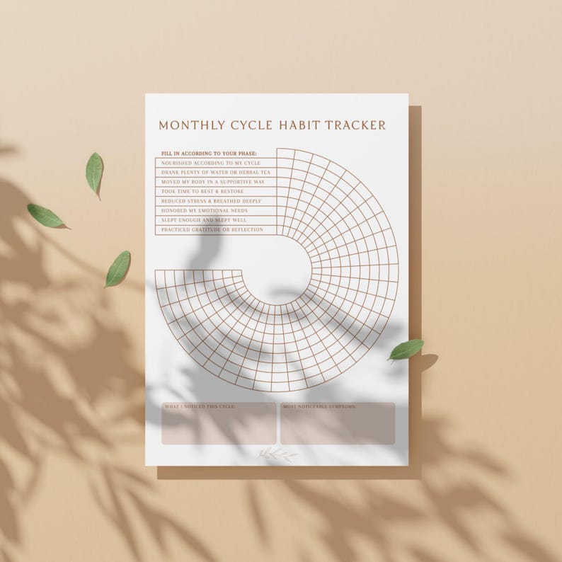 May include: A habit tracker with the text "MONTHLY CYCLE HABIT TRACKER". The design features a circular grid for tracking habits, with prompts for self-care. The paper is white, set against a light brown background, with green leaves.