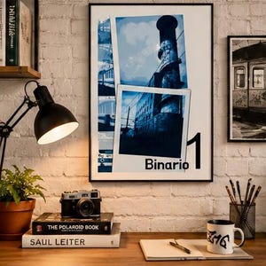 Könnte beinhalten: Ein gerahmter Wandkunstdruck mit einer Collage aus blautönigen Fotografien eines Bahnhofs und eines hohen Schornsteins, mit dem in Schwarz gedruckten Text Binario 1. Das Kunstwerk befindet sich in einem dünnen schwarzen Rahmen an einer weißen Backsteinwand.