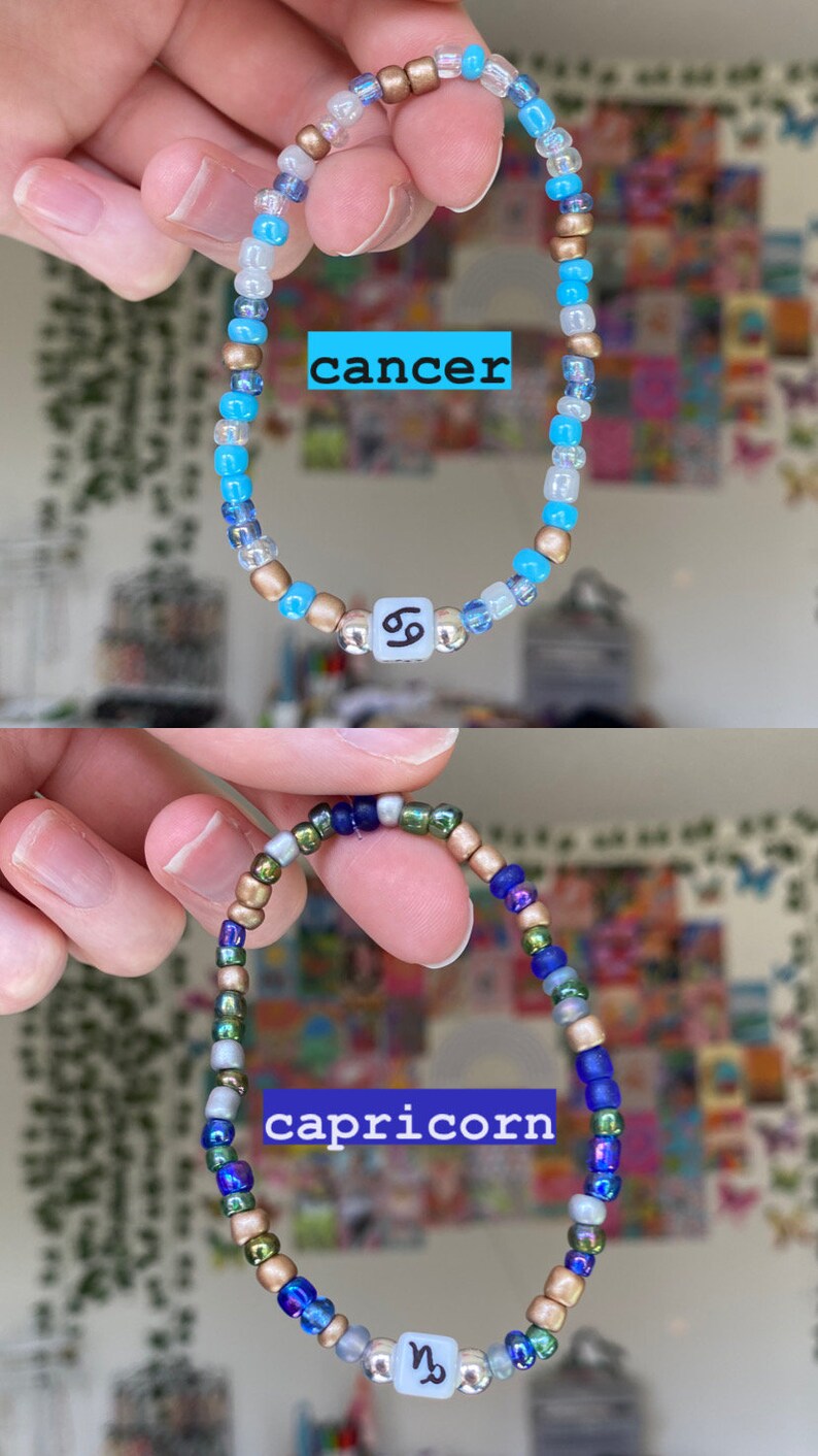 May include: Two beaded bracelets, one blue and gold with "cancer" text, the other blue, green, and gold with "capricorn" text. Each bracelet has a zodiac symbol bead. The bracelets are held up.