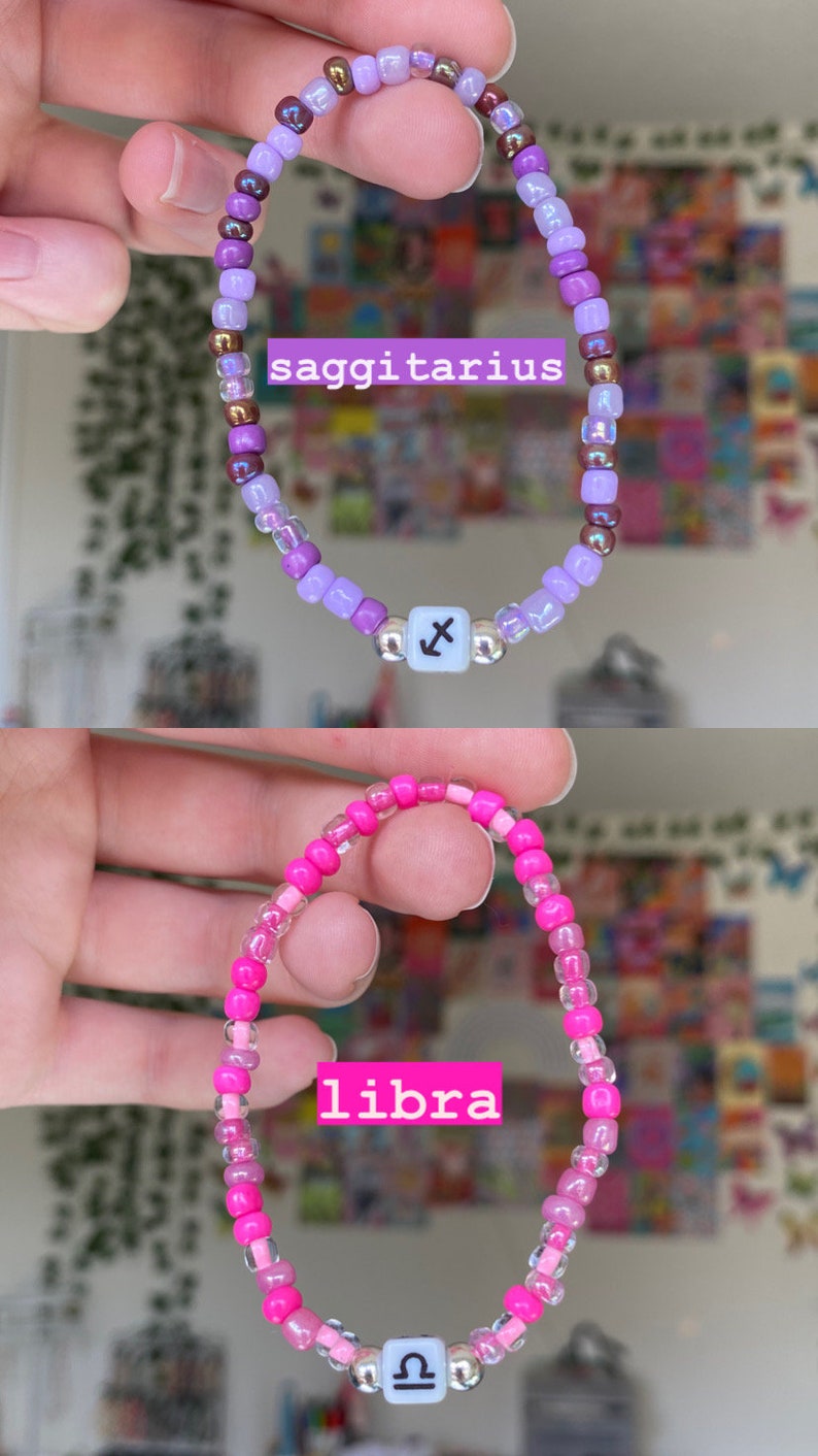 May include: Two beaded bracelets, one purple and one pink. The purple bracelet says "saggitarius" and has a Sagittarius symbol bead. The pink bracelet says "libra" and has a Libra symbol bead. Both bracelets are held up.