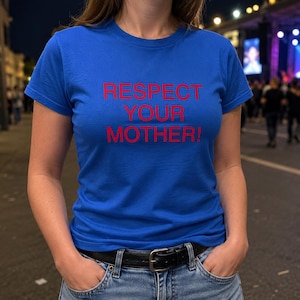 May include: A bright blue short-sleeved t-shirt featuring the text "RESPECT YOUR MOTHER!" printed in bold red capital letters across the chest. The shirt has a crew neckline and is worn tucked into blue denim jeans with a black leather belt.