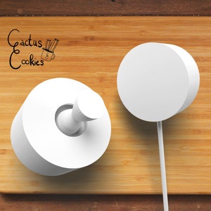 May include: Two white fondant cookie cutters, one round and one shaped like a donut with a hole in the center. The cutters are on a wooden surface.