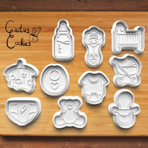 May include: Set of 10 white plastic baby shower cookie cutters, including a baby bottle, rattle, crib, pacifier, diaper, teddy bear, baby mobile, onesie, bib, and stroller.