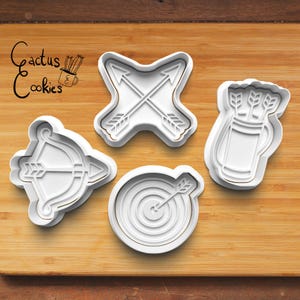 Puede incluir: Cuatro cortadores de galletas blancos con formas de arquería: un arco y flecha, flechas cruzadas, un carcaj de flechas y una diana con una flecha. Los cortadores de galletas están sobre una superficie de madera, con el texto "Cactus Cookies".