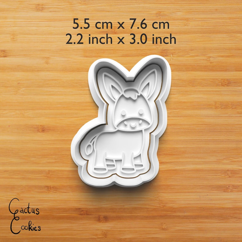Puede incluir: Cortador de galletas blanco con forma de burro, de 5,5 cm por 7,6 cm (2,2 pulgadas x 3,0 pulgadas). El dise&ntilde;o presenta un burro sonriente con orejas grandes y una cola peque&ntilde;a. El texto "Cactus Cookies" est&aacute; en la esquina inferior izquierda.