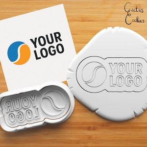 Op de afbeelding: Witte plastic koekjesvormer met een blauw en oranje logo met de tekst "YOUR LOGO".