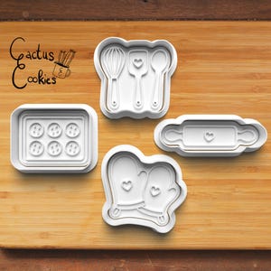 May include: White plastic cookie cutters in various kitchen-themed shapes, including a whisk, spatula, spoon, rolling pin, oven mitts, and a tray of six circles. The text "Cactus Cookies" is in the upper left corner.