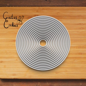 May include: A set of 12 round metal cookie cutters, nested in size, on a wooden surface. The cutters are silver in colour and range in size from small to large.