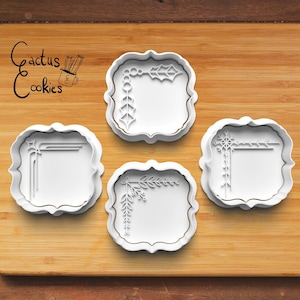 May include: Four white plastic cookie cutters with different corner designs. Each cutter features a decorative border and a blank space in the center. The cutters are arranged on a wooden surface.