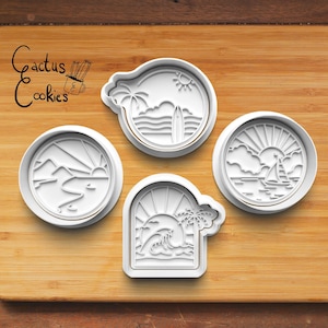 Puede incluir: Cuatro cortadores de galletas de plástico blanco con forma de diferentes escenas de playa. Los cortadores están sobre una superficie de madera. Los cortadores presentan una palmera, una tabla de surf, un velero, una montaña y un sol.