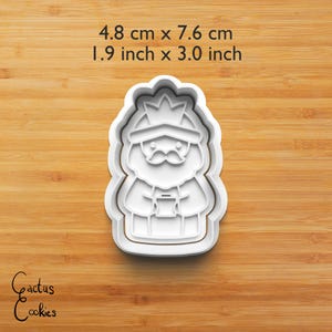Puede incluir: Cortador de galletas de pl&aacute;stico blanco con forma de rey, de 4,8 cm por 7,6 cm. El rey tiene una corona y bigote, sosteniendo un objeto peque&ntilde;o. El texto "Cactus Cookies" est&aacute; en la esquina inferior izquierda.