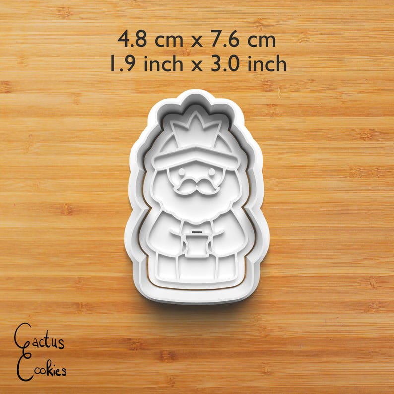 Puede incluir: Cortador de galletas de pl&aacute;stico blanco con forma de rey, de 4,8 cm por 7,6 cm. El rey tiene una corona y bigote, sosteniendo un objeto peque&ntilde;o. El texto "Cactus Cookies" est&aacute; en la esquina inferior izquierda.