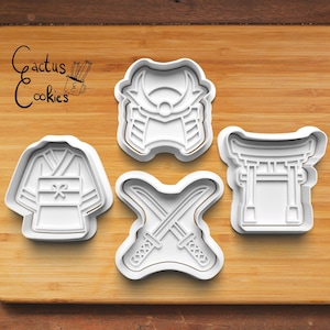 Peut inclure: Quatre emporte-pièces en plastique blanc représentant des symboles culturels japonais. Les formes comprennent un kimono, une armure de samouraï, des épées croisées et une porte torii. Le logo Cactus Cookies est dans le coin supérieur gauche.