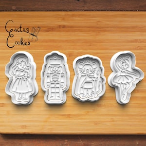 Può includere: Quattro formine per biscotti in plastica bianca a forma di personaggi del balletto Lo Schiaccianoci. Le forme includono una ragazza, un soldato schiaccianoci, un re topo e una ballerina. Le formine sono su una superficie di legno.