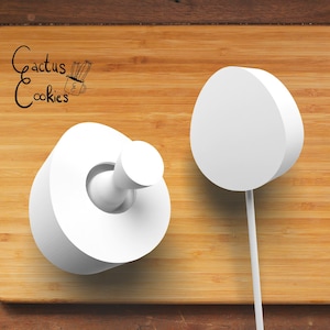 May include: Two white cake pops on a wooden surface. The cake pops are round and have a smooth surface. The cake pop on the left has a small round indentation in the center. The cake pop on the right is on a stick.