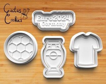 Op de afbeelding: Vier witte plastic koekjesvormen, gevormd als een voetbal, een trofee, een t-shirt en een banner met de tekst "Euro 2024 Duitsland".