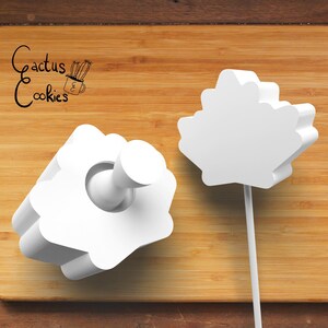 Puede incluir: Dos cortadores de galletas blancos en forma de flor sobre una superficie de madera. Uno tiene un mango y el otro está en un palo. El texto "Cactus Cookies" está en la esquina superior izquierda, con una pequeña ilustración de cactus.