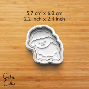 Puede incluir: Un cortador de galletas blanco con forma de oveja, que mide 5,7 cm por 6,0 cm (2,2 pulgadas x 2,4 pulgadas). El cortador presenta un contorno detallado de una oveja con un cuerpo esponjoso y una cara sonriente. El texto "Cactus Cookies" est&aacute; en la esquina inferior izquierda.