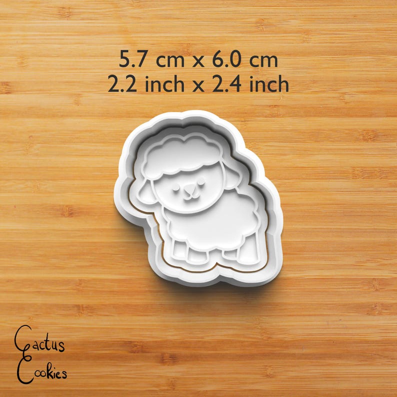 Puede incluir: Un cortador de galletas blanco con forma de oveja, que mide 5,7 cm por 6,0 cm (2,2 pulgadas x 2,4 pulgadas). El cortador presenta un contorno detallado de una oveja con un cuerpo esponjoso y una cara sonriente. El texto "Cactus Cookies" est&aacute; en la esquina inferior izquierda.