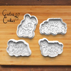 May include: Four white plastic cookie cutters with the text "Happy Easter" in different styles. The cutters are on a wooden surface.