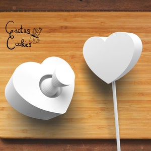 Puede incluir: Dos cortadores de galletas en forma de corazón blanco sobre una superficie de madera. Un cortador tiene un agujero redondo en el centro, el otro es una simple forma de corazón.