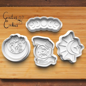 Puede incluir: Cuatro cortadores de galletas de plástico blanco sobre una superficie de madera. Los cortadores tienen forma de media luna, cristal y luna, mano sosteniendo una bola de cristal y sol y luna.