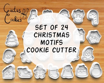 Puede incluir: Conjunto de 24 cortadores de galletas de Navidad de plástico blanco sobre una superficie de madera. Los cortadores incluyen un árbol de Navidad, Santa Claus, un muñeco de nieve, un hombre de jengibre, una media, un regalo, un copo de nieve, un bastón de caramelo, un ángel, una estrella, una campana, un trineo, una casa y un reno.