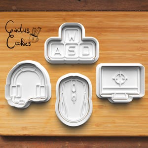 May include: Set of five white plastic cookie cutters shaped like gaming icons: a headset, a mouse, a keyboard with the keys WASD, and a computer monitor with a target in the center.
