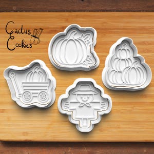 Op de afbeelding: Vier witte plastic koekjessnijders in herfstvormen: een pompoen, een stapel pompoenen, een pompoen in een wagen en een vogelverschrikker. De afbeelding bevat de tekst "Cactus Cookies" in een scriptlettertype.