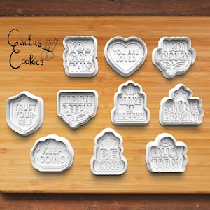 May include: Ten white plastic cookie cutters with various positive messages, including "You Got This", "Breathe Deeply", "Make It Happen", and "Shine Bright".