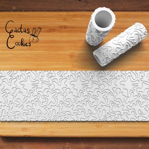 May include: Two white rolling pins with a textured, abstract design. The rolling pins are on a wooden chopping board. The design on the rolling pins is also visible on a white strip of material on the chopping board.