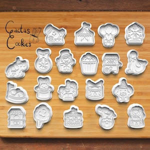 Puede incluir: Un juego de cortadores de galletas de plástico blanco con formas de temática circense que incluyen un cañón, una carpa, globos, una noria, un elefante, un monociclo, un maestro de ceremonias, palomitas, un carrito, una foca, un coche de choque, un conejo en un sombrero, un caballo de tiovivo, un tambor, un payaso, un puesto, algodón de azúcar, un tiovivo y un león.