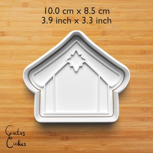 Puede incluir: Cortador de galletas de pl&aacute;stico blanco con forma de casa con una estrella en el tejado. El cortador mide 10,0 cm por 8,5 cm (3,9 pulgadas por 3,3 pulgadas). Las palabras "Cactus Cookies" est&aacute;n escritas en cursiva en la parte inferior izquierda.