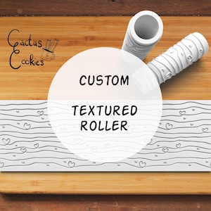 Pode incluir: Um rolo texturizado personalizado branco com um padrão de coração, sobre uma superfície de madeira. O rolo tem uma pega cilíndrica e uma superfície de rolagem estampada. A imagem também apresenta o texto "Custom Textured Roller".