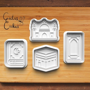 Peut inclure: Quatre emportes-pièces en plastique blanc en forme de symboles religieux islamiques : une mosquée, un livre, un tapis de prière et la Kaaba. Les emportes-pièces sont sur une surface en bois.