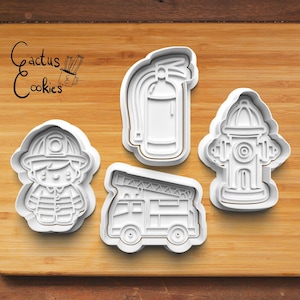 May include: Four white plastic cookie cutters shaped like a firefighter, a fire truck, a fire hydrant, and a fire extinguisher. The cutters are on a wooden surface.