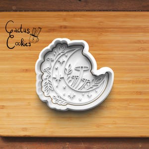 Puede incluir: Cortador de galletas de plástico blanco en forma de media luna con un diseño detallado de hojas, setas y estrellas.