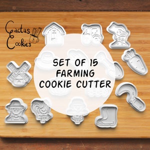 May include: Set of 15 white plastic cookie cutters shaped like farm animals, vegetables, and farm equipment. The cutters are arranged on a wooden surface. The text "SET OF 15 FARMING COOKIE CUTTER" is printed on a white circle in the center of the image.